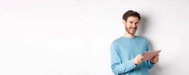 E-ticaret ve teknoloji konsepti. Kameraya gülümseyen, elinde dijital tabletle beyaz arka planda duran beyaz bir adam..