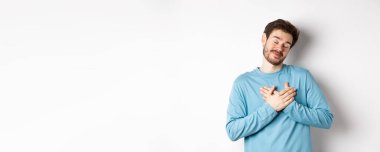 Yakışıklı genç adam romantik hissediyor, kalbi tutuyor ve güzel güzel anıları düşünüyor, beyaz arka planda duruyor..