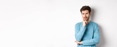 Genç sakallı adam düşünceli ve somurtuyor, sorun ya da sorun hakkında düşünüyor, beyaz arka plana karşı endişeli duruyor..