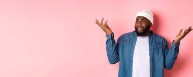 Şüpheci şaşkın adam saçma bir şeye bakıyor, sola bakıyor ve omuz silkiyor, kafası karışmış, pembe arka planda duruyor..