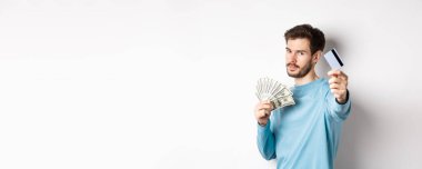 Ciddi görünümlü bir adam plastik kredi kartıyla elini uzatıyor, para yerine temassız ödemeyi tercih ediyor, beyaz arka planda duruyor..