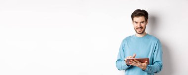 E-ticaret. Gülümseyen beyaz adam dijital tablet kullanıyor ve beyaz arka planda duran kameraya bakıyor..