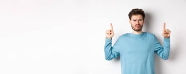 Hayal kırıklığına uğramış erkek model somurtuyor, olumsuz duygularla parmakla işaret ediyor, tanıtım teklifinden hoşlanmıyor, beyaz arka planda duruyor..