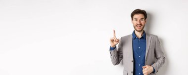 Heyecanlı takım elbiseli işadamı iyi fikir sunuyor, Eureka işaretinde parmağını kaldırıyor ve komik görünüyor, öneriler söylüyor, beyaz arka planda duruyor..