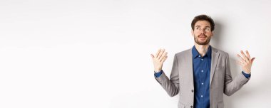 Takım elbiseli genç yöneticinin biraz havaya ihtiyacı var. Kızarık ve sinirli hissederek el sallıyor. Beyaz arka planda duruyor..