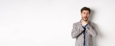 Takım elbiseli sıkıntılı genç adam kendini boğar ve dilini gösterir. Boğazı ağrır, beyaz arka planda durur..