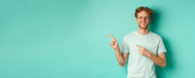 Kısa kızıl saçlı ve gözlüklü neşeli genç adam, parmaklarını fotokopi alanına gösteriyor, gülümseyen beyaz dişler, reklam gösteriyor, nane arkaplanı..
