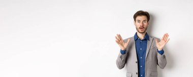 Süpriz takım elbiseli işadamı elini kaldırıyor ve heyecanlı görünüyor, beyaz arka plana karşı duruyor..