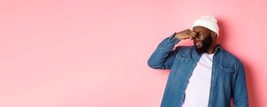 İğrenç Afro-Amerikalı adam tiksinti duymaz, kötü kokudan rahatsız olur, pembe arka planda bereli ve kot gömlekli dikilir..