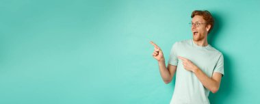 Kızıl saçlı, gözlüklü ve tişörtlü heyecanlı genç adam, harika bir terfiyi işaret ediyor ve sola bakıyor, afişte mutlu gülümsüyor, turkuaz arka plan.