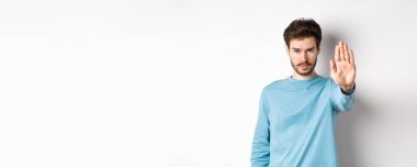 Ciddi genç adam elini uzatmış kendine güveniyor, dur diyor, kötü bir şeyi yasaklıyor ya da beyaz arka planda dikilip uyarı veriyor..