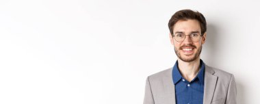 Gözlüklü, takım elbiseli, kameraya gülümseyen, beyaz arka planda mutlu görünen genç ofis çalışanlarının yakın çekimi..