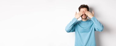 Gülümseyen beyaz adam sürpriz bekliyor, gözleri kapalı, hediye bekliyor, beyaz arka planda duruyor. Kutlama ve tatil kavramı.