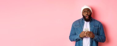 Teknoloji ve online alışveriş konsepti. Kafası karışmış ve hayal kırıklığına uğramış Afro-Amerikan adam şikayet ediyor, cep telefonunu tutuyor ve kameraya bakıyor..