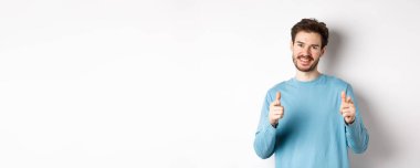 İyi iş çıkardın. Tebrik etmek ya da övmek için kamerayı gösteren gülümseyen yakışıklı adam beyaz arka planda gururlu bir şekilde duruyor..