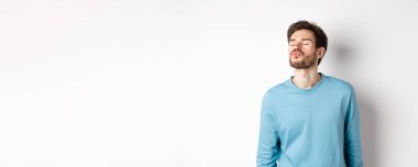 Öpüşmeyi bekleyen tatlı ve aptal bir adamın görüntüsü, dudakları büzüşmüş, gözleri kapalı, beyaz arka planda duruyor..