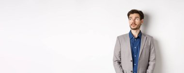 Takım elbiseli düşünceli üzgün işadamı sol üst köşedeki logoya bakıyor, düşünüyor veya uzaklaşıyor, beyaz arka planda duruyor..