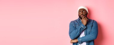 Şüpheli Afrikalı Amerikalı adam sol üst köşeye bakıyor düşünceli, karar veriyor ve düşünüyor, pembe arka planda duruyor..