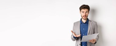 Kafası karışmış işadamı kötü belgeye bakıyor, anlaşmadan şikayet ediyor, kağıt üzerinde hayal kırıklığına uğramış, beyaz arka planda takım elbise içinde duruyor..