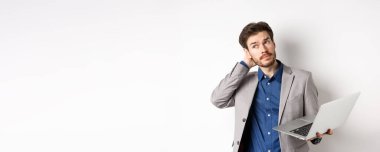 Düşünceli işadamı başını kaşıyarak başını çeviriyor, laptopta çalışırken karar veriyor, beyaz arka plana karşı duruyor..