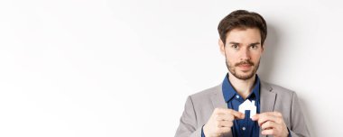 Gayrimenkul ve sigorta konsepti. Satıcı emlakçı, küçük kağıt ev resimlerini gösteriyor ve kameraya bakıyor, mülk satıyor, beyaz arka plan..