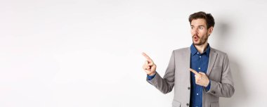 Vay canına, şuraya bak. Heyecanlı erkek yönetim kurulu başkanı sol parmaklarını işaret ederek logoya bakıyor, reklamını yapıyor, beyaz arka planda duruyor..