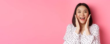 Güzel Asyalı bir kadının temiz cilde dokunuşunu ve kameraya şaşkın şaşkın bakıp pembe arka planda duruşunu yakından çek..