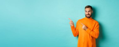 Hoşnutsuz bir adam kötü bir şeyden korkup iğrenç ya da garip bir şeye bakar, sol tarafta fotokopi alanı, turkuaz arka planda durur..