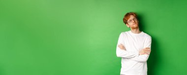 Kızıl saçlı, gözlüklü, sağ taraftaki fotokopi odasında kendini beğenmiş, göğsünde kendinden emin, yeşil arka planda duran kendine güvenen genç bir adam..