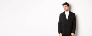 Takım elbiseli yorgun bir adamın hüzünlü, kasvetli bir ifadeyle sol tarafa bakması, fotokopi alanına bakması, beyaz arka planda bitkin bir şekilde durması..