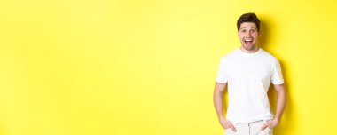 Adam şaşırmış görünüyor, gülümsüyor ve anonsa bakıyor, fotokopi alanının yanında duruyor, sarı arkaplan.