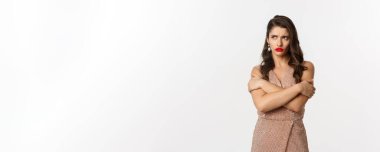 Kutlama ve parti konsepti. Kızgın suratlı bir kadın, resmi bir tören için giyinmiş, kendine sarılıyor ve üzgün somurtuyor, beyaz arka planda..