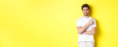 Şüpheci ve keyifsiz bir adam topal, isteksiz, sarı arka planda duran bir şeyi işaret ediyor..