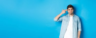 Sıkıntıdan kendini vuran, mavi arka planda duran yorgun ve rahatsız yetişkin bir adam parmak tabancasıyla başını işaret ediyor..