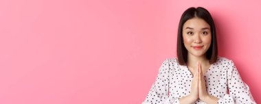 Güzellik ve yaşam tarzı konsepti. Hoş Asyalı bir kadının gülümsemesi, teşekkür jesti göstermesi, dua etmesi, pembe arka planda durması..