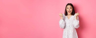 Asyalı güzel bir kadının kazandığını, yumruklarını sıktığını ve mutlu bir yüzle evet dediğini zafer kazandığını ve pembe arka planda dikildiğini hayal et..