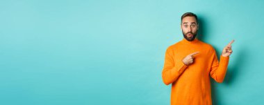 Reklam veren, pankartı işaret eden, turkuaz arka planda duran harika bir adam..
