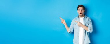 Gözlüklü şaşırmış bir adam fotokopi alanını işaret ediyor, ürün hakkında sorular soruyor, ilgi çekici görünüyor, mavi arka planda duruyor..