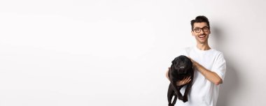 Gözlüklü, evcil köpekli ve gülümseyen hippi. Şirin siyah pug sahibi ile vakit geçirmeyi seviyor, tatmin olmuş görünüyor, beyaz arka planda duruyor..