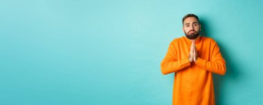 Somurtkan adam yardım dileniyor, iyilik istiyor, el ele tutuşup dua ediyor ve somurtuyor, turkuaz arka planda duruyor..