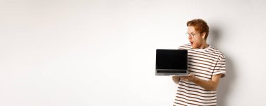 Genç kızıl saçlı adam etkilenmiş görünüyor. Bilgisayarında logo pankartı olan boş bir ekran gösteriyor. Gözlüklü adam bilgisayardaki internet reklamını kontrol ediyor, beyaz arka plan..