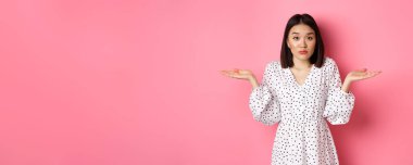 Belirsiz şirin Asyalı kadın omuz silkiyor, el ele tutuşuyor, fotokopi alanlarında yayılıyor, bilmiyorum, şüpheleri var, pembe arka planda duruyor..