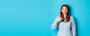 Umut dolu kızıl kız kendini işaret ediyor, mavi arka planda duruyor..