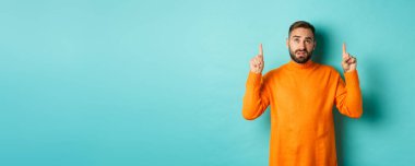 Şüpheli ve keyifsiz görünen bir adam, hoş olmayan bir şeyi işaret ediyor, turkuaz arka plana şüpheyle bakıyor..