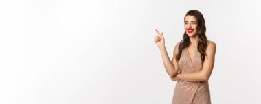 Noel, tatiller ve kutlama konsepti. Parti elbisesi giyen çekici bir kadın ve kırmızı ruj, işaret eden ve sola bakan, yeni yıl arifesinde beyaz arka plan.