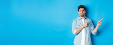 Şüpheci yetişkin adamın portresi, parmaklarını sağa ve sırıtarak, hayal kırıklığını ve şüpheyi dışa vurarak, mavi arka planda duruyor..