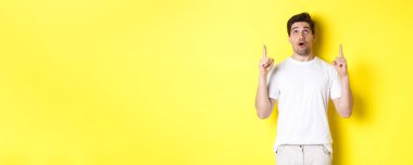 Etkilenmiş adam reklam teklifini kontrol ediyor, bakıyor ve işaret ediyor, sarı arka planda duruyor..