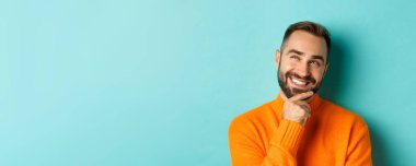 Kafkas erkek modelinin yakın plan bir fikri var, gülümsüyor ve sol üst köşeye bakıyor düşünceli, görüntüleme planı, açık mavi arka planda duruyor..