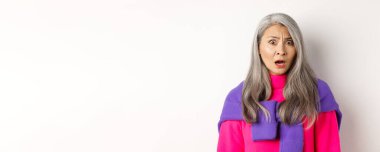 Şok olmuş Asyalı son sınıf öğrencisinin yakın çekimleri, kafası karışmış bir şekilde bakan, korkuyla bakan, beyaz arka plana karşı duran.