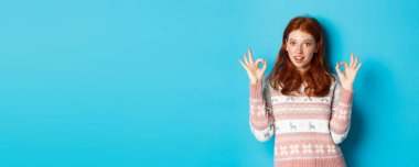 Kendine güveni tam kızıl saçlı bir kadının görüntüsü. Her şeyin yolunda olduğuna emin, övgüyle seçilmiş, mavi arka planda duruyor..